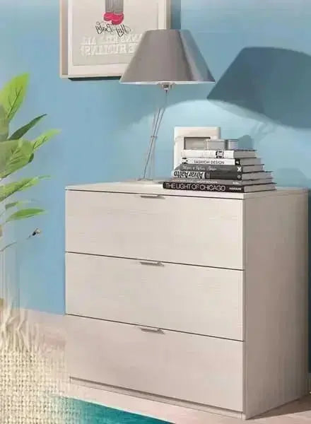 Cassettiera in rovere con 3 cassetti posizionata in un soggiorno moderno con parete blu, decorata con lampada, libri e pianta. Ideale per archiviazione elegante.