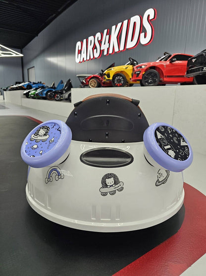 Auto per bambini con volante e sedile in pelle marrone, decorata con personaggi e simboli spaziali, in un'area espositiva di giochi