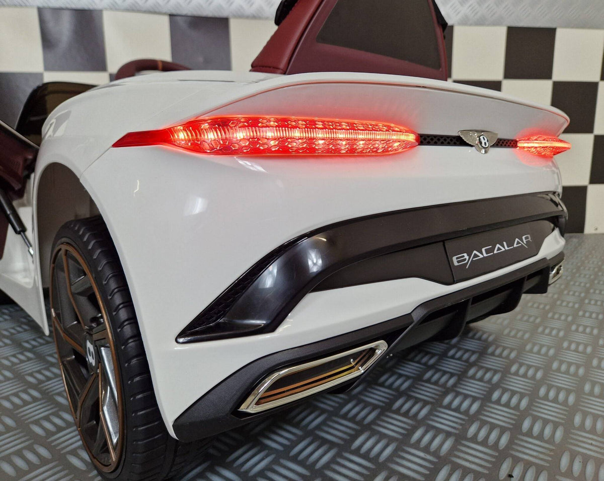 Vista frontale dell'auto elettrica per bambini Bentley Bacalar bianca, con fari anteriori accesi e dettagli di design di lusso, in ambiente con pavimento a scacchi.