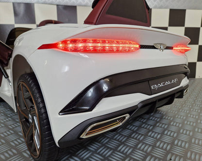 Vista frontale dell'auto elettrica per bambini Bentley Bacalar bianca, con fari anteriori accesi e dettagli di design di lusso, in ambiente con pavimento a scacchi.