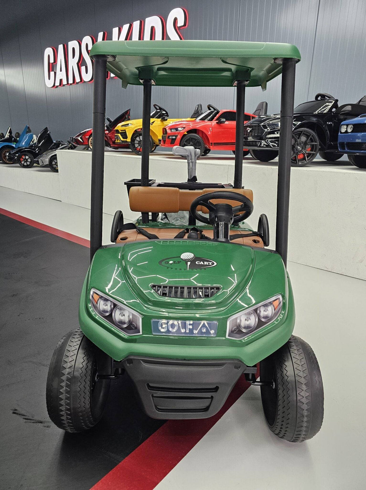 Vista frontale del carrello da golf elettrico per bambini verde con dettagli in plastica nera, luci anteriori e logo GOLF