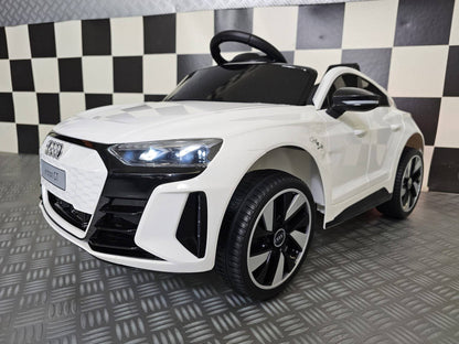 Vista frontale dell'auto per bambini Audi E-Tron bianca con fari LED accesi, dettagli neri, griglia frontale e ruote grandi in plastica