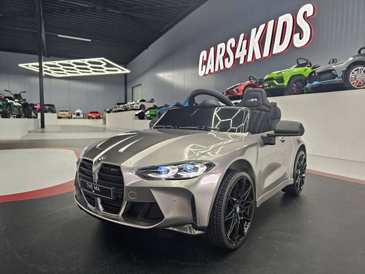 Auto elettrica per bambini BMW M4 in grigio metallizzato, con dettagli realistici, sedile, volante e luci LED, dimensioni compatte.