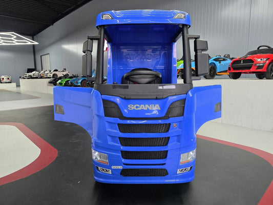 Vista frontale del camion elettrico per bambini blu con dettagli di griglia e logo Scania, in esposizione con auto sportive colorate sullo sfondo