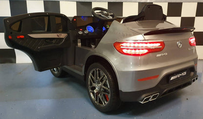 Interno dell'auto elettrica per bambini Mercedes GLC 63 AMG, con volante, pannello di controllo e sedile in pelle nera.