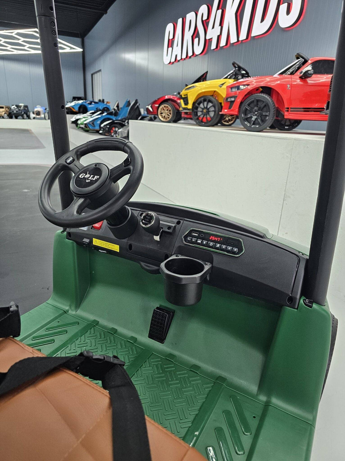 Carrello da golf elettrico per bambini 24 V con sedile in pelle marrone, volante nero, e spazio per mazze da golf e palline, in un centro commerciale
