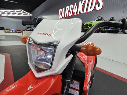 Fronte della moto elettrica Honda CRF 12V rossa con fari LED e dettagli di design, in mostra con sfondo di auto giocattolo