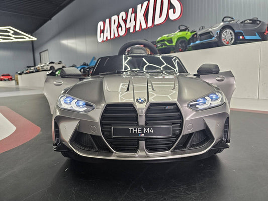 Vista frontale dell'auto elettrica per bambini BMW M4 in grigio metallizzato, con fari LED e dettagli di design sportivo.