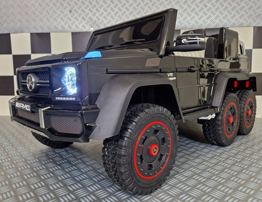 Vista frontale dell'auto elettrica per bambini Mercedes G63 AMG 6x6 in nero, con fari LED accesi, griglia frontale e dettagli autentici, ideale per divertimento sicuro.