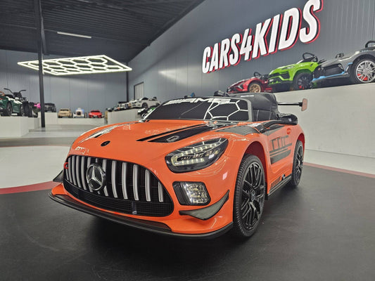 Auto elettrica per bambini Mercedes AMG GT3 in colore arancione con dettagli neri, volante e sedile, ideale per giochi all'aperto