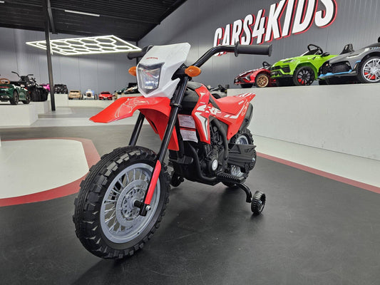 Moto elettrica per bambini Honda CRF 12V rossa con pneumatici tassellati, manubrio nero e fari anteriori, in esposizione in showroom