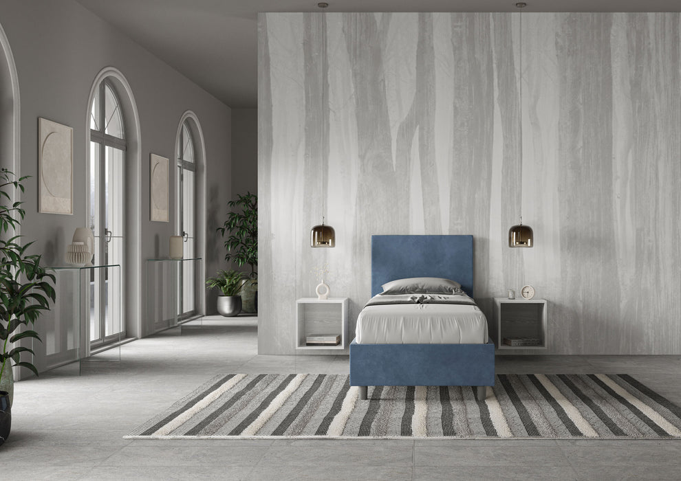Letto singolo imbottito Adele 80x210 blu navy in microfibra, inserito in ambiente elegante con tappeto a righe e pareti grigie.