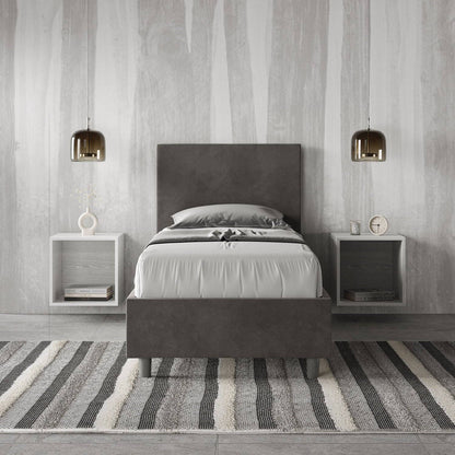 Letto singolo contenitore imbottito 90x200 microfibra Adele grigio scuro in camera moderna. Arredo elegante con comodini sospesi e tappeto a righe.
