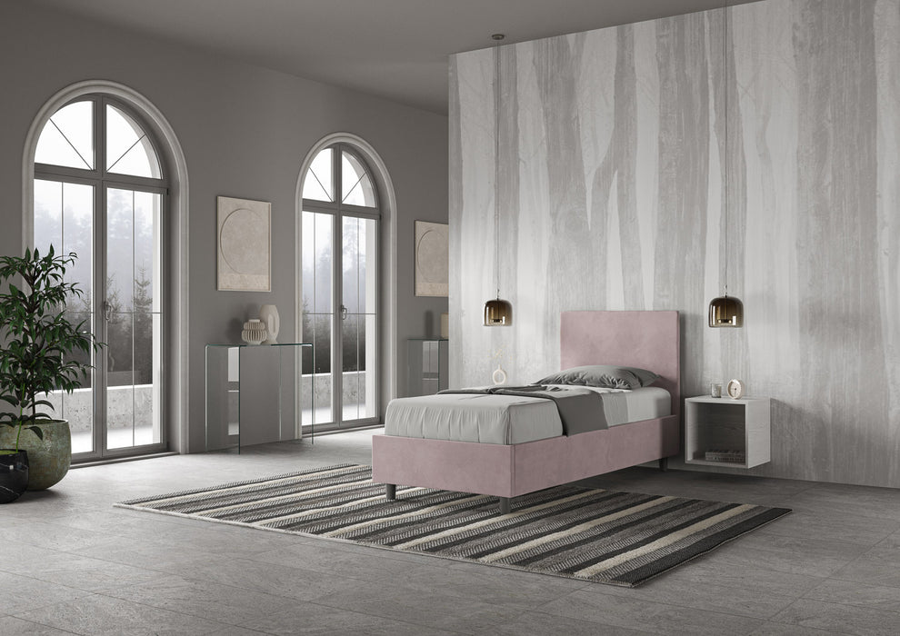 Letto singolo Adele 80x190 rosa cipria senza contenitore, ambientato in una stanza luminosa con arredamento minimal e tappeto a righe.