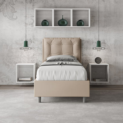 Letto singolo Annalisa beige in similpelle con testata imbottita, collocato in una camera moderna con mensole e illuminazione sospesa.