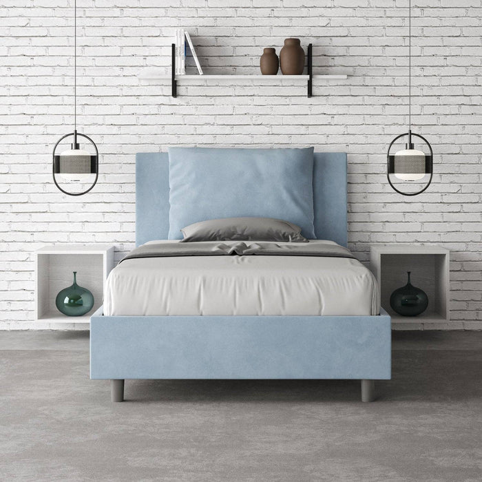 Letto singolo Antea azzurro 100x200 con contenitore, ambientato in una camera minimalista con parete in mattoni bianchi.