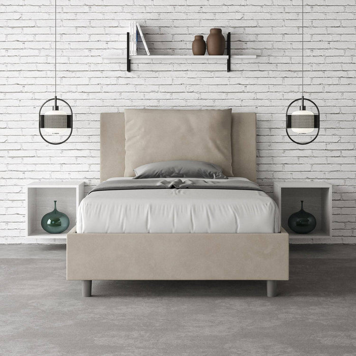 Letto singolo Antea beige con contenitore, inserito in una camera minimal con parete in mattoni bianchi e arredi sospesi.