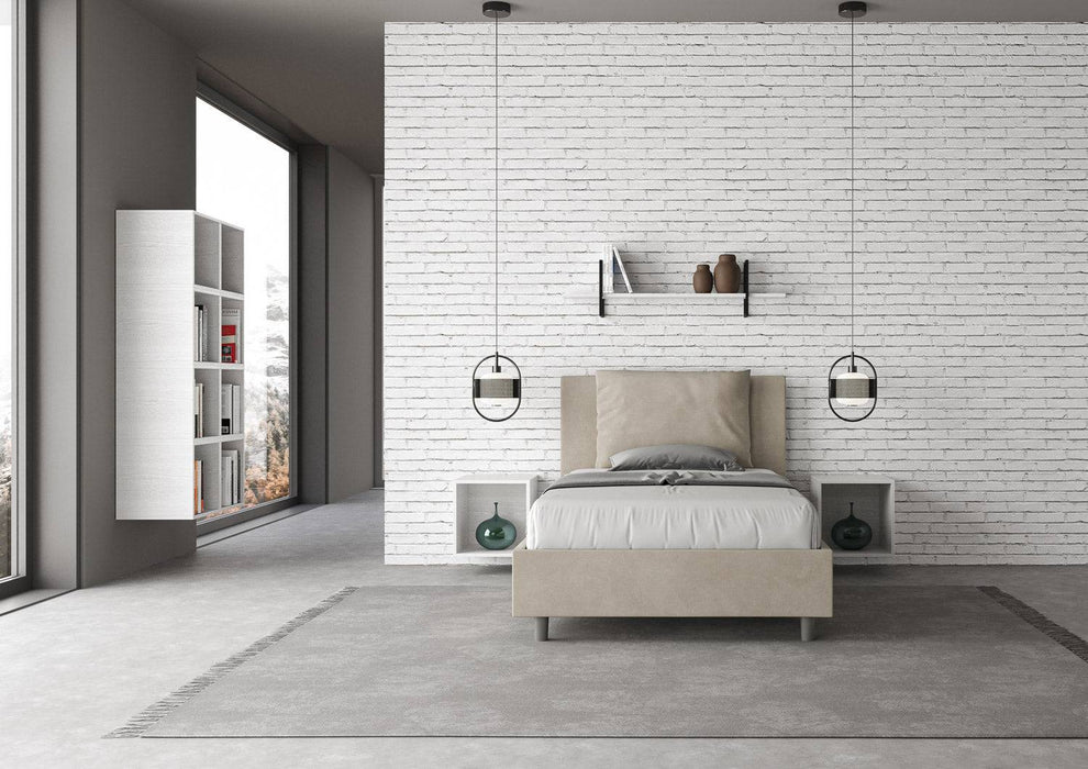 Letto singolo contenitore imbottito 100x210 microfibra Antea beige in stanza con parete bianca e arredi sospesi. Design essenziale e pratico.