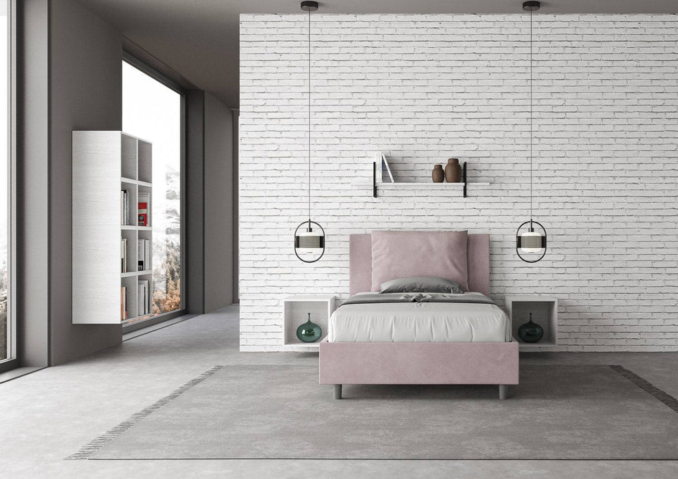 Letto singolo Antea rosa cipria con contenitore, inserito in una camera luminosa con parete in mattoni bianchi e arredi sospesi.