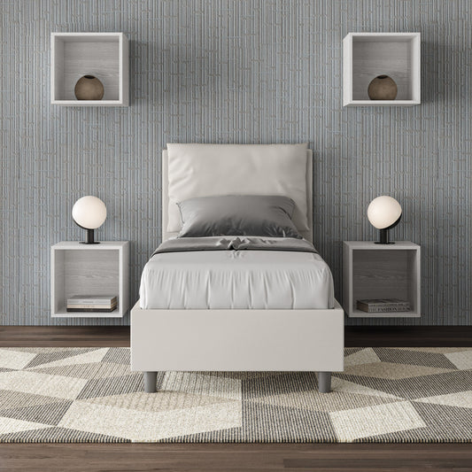 Letto singolo Antea bianco in similpelle con rete, inserito in una camera moderna con parete grigia e arredi geometrici.