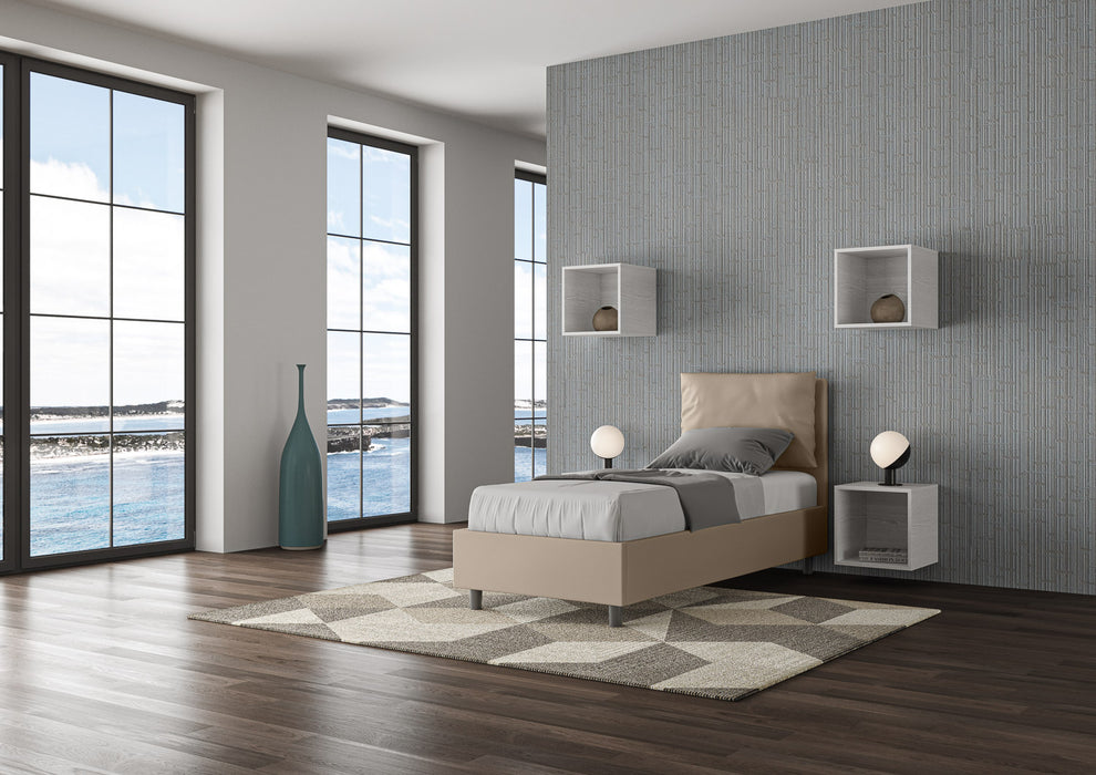 Letto singolo imbottito Antea beige in similpelle con contenitore, perfetto per camere moderne con ampie finestre e luce naturale.