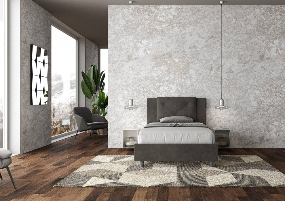 Letto singolo contenitore imbottito 100x200 microfibra Appia in grigio scuro, inserito in un ambiente moderno con parquet e pareti chiare.
