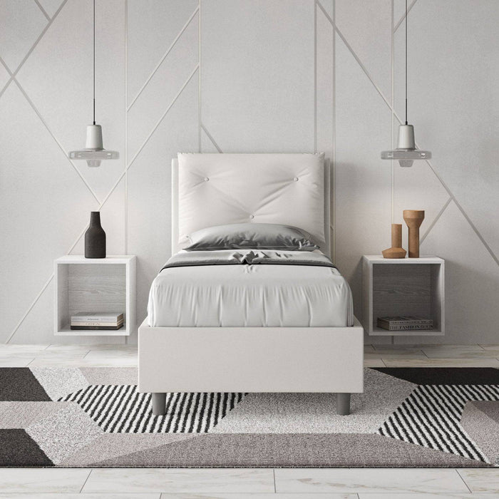 Letto singolo 80x200 in similpelle bianca con testiera trapuntata, inserito in una camera moderna con comodini sospesi.
