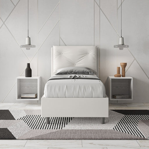 Letto singolo Appia bianco in similpelle con testiera imbottita, inserito in camera moderna con comodini sospesi e tappeto geometrico