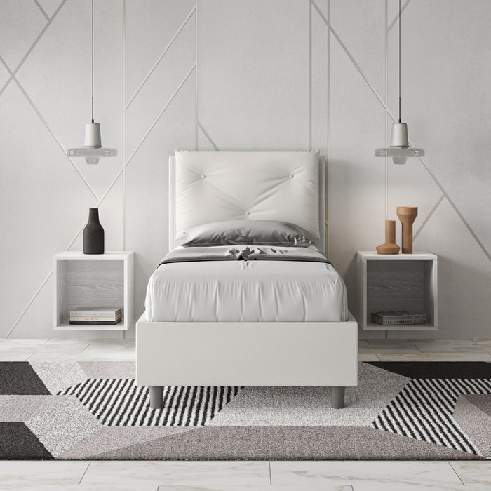 Letto singolo Appia bianco in similpelle con testiera imbottita, inserito in camera moderna con comodini sospesi e tappeto geometrico