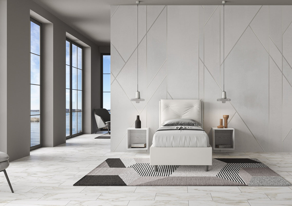 Letto singolo imbottito Appia bianco in similpelle, ambientato in stanza luminosa con vista mare e arredamento contemporaneo