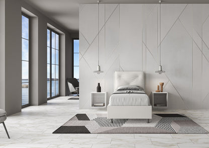 Letto singolo imbottito Appia bianco in similpelle, ambientato in stanza luminosa con vista mare e arredamento contemporaneo