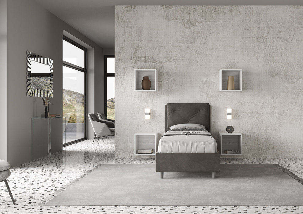 Letto singolo Appia grigio antracite 80x190 con struttura imbottita, posizionato in una camera luminosa con arredi sospesi e vista esterna.