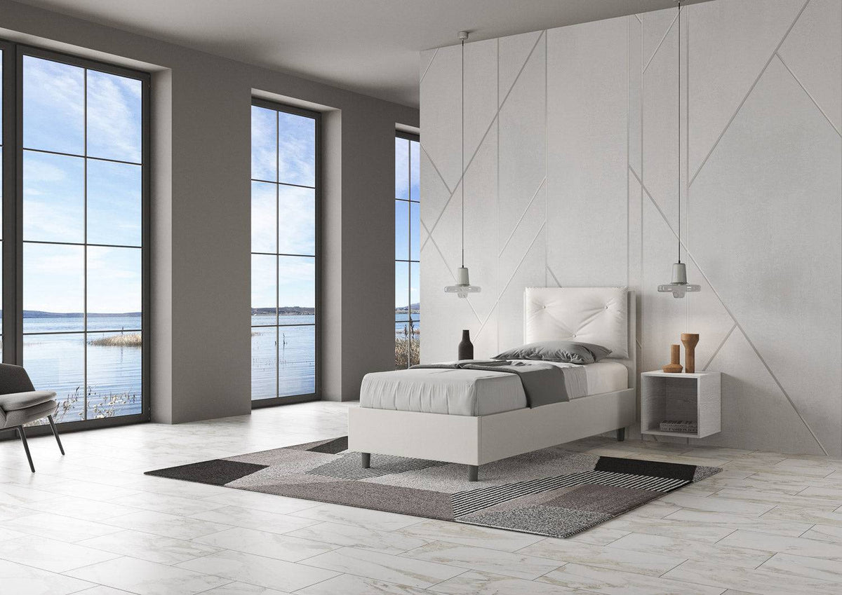 Letto singolo 80x200 in similpelle bianca con testiera trapuntata, posizionato in una stanza luminosa con vista panoramica.