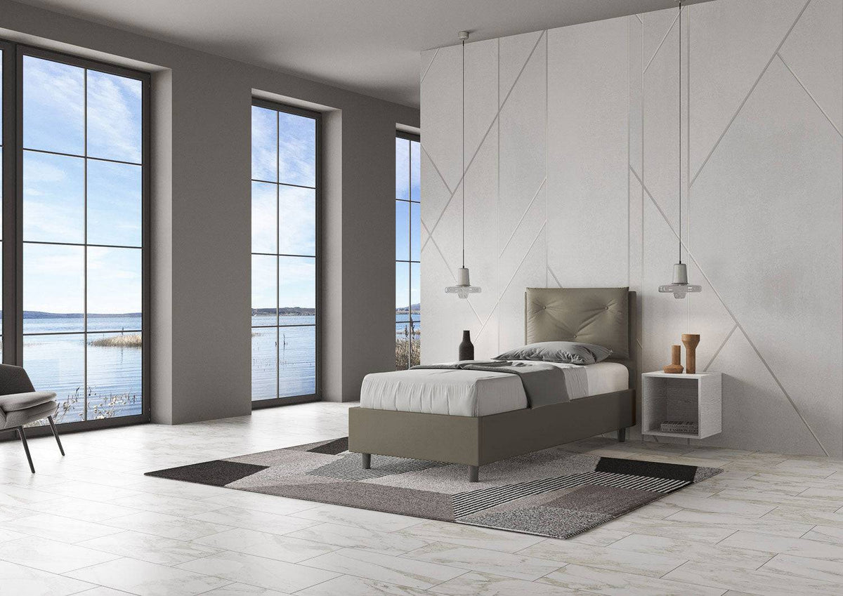 Letto singolo 80x200 in similpelle grigia con testiera trapuntata, posizionato in una stanza luminosa con vista panoramica.