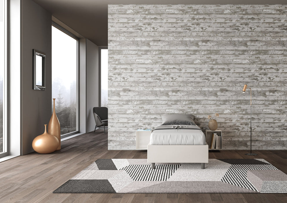 Letto singolo Azelia grigio tortora in similpelle, ambientato in camera con pareti effetto cemento e tappeto geometrico