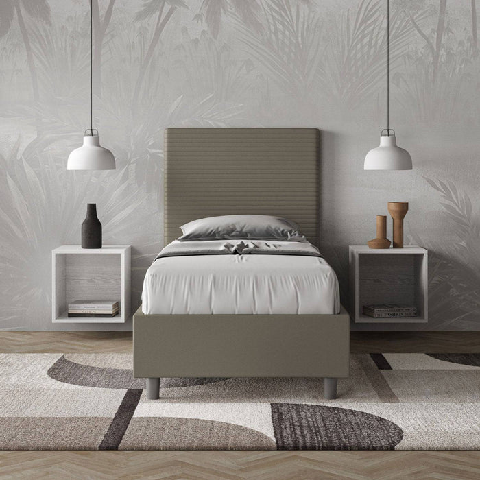 Letto singolo contenitore Focus grigio in similpelle, inserito in una camera elegante con comodini sospesi e tappeto geometrico.