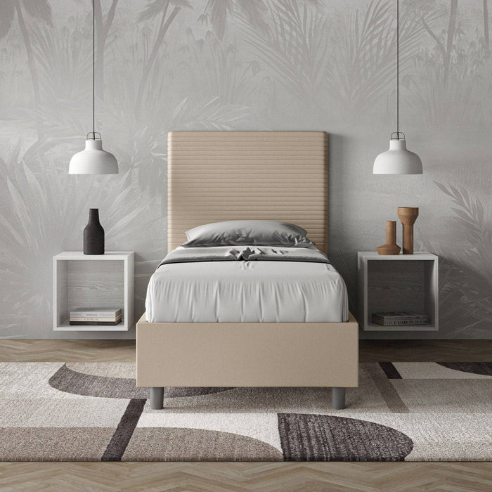 Letto Focus 90x200 in similpelle beige con contenitore, ambientato in una camera elegante con comodini sospesi e tappeto decorativo.