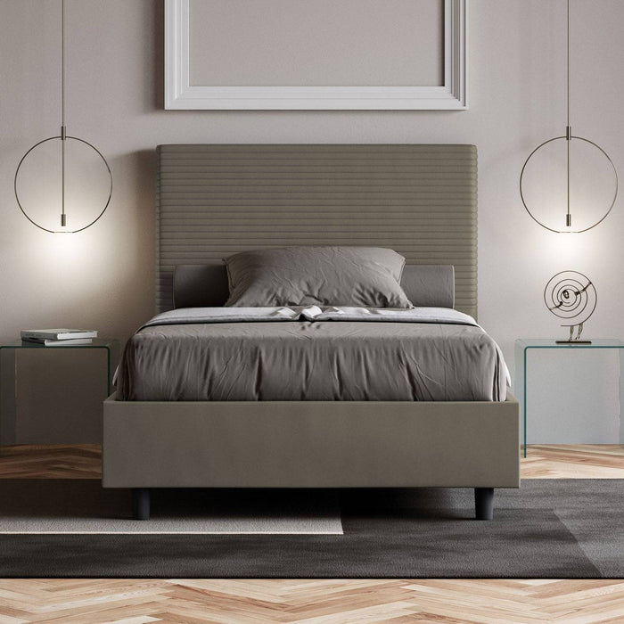 Letto singolo Focus in similpelle grigia con contenitore, inserito in una camera elegante con illuminazione sospesa e parquet.