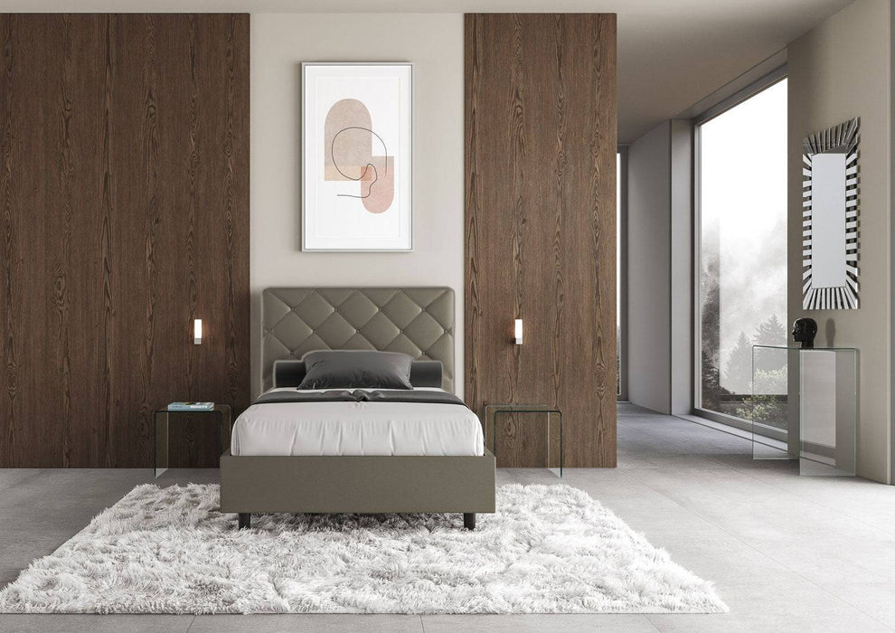 Letto singolo contenitore Priya grigio in similpelle in una camera moderna con pareti in legno e tappeto bianco.