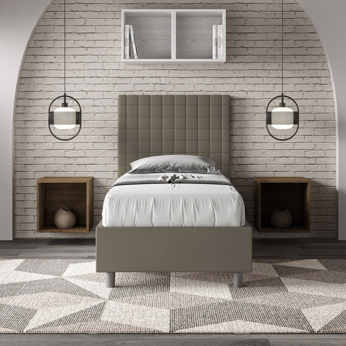 Letto singolo imbottito similpelle Sunny grigio scuro in camera moderna con parete in mattoni. Arredo elegante per ambienti raffinati.