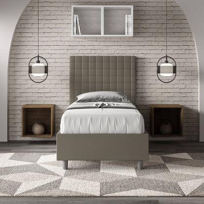Letto singolo imbottito similpelle Sunny grigio scuro in camera moderna con parete in mattoni e comodini in legno incassati.