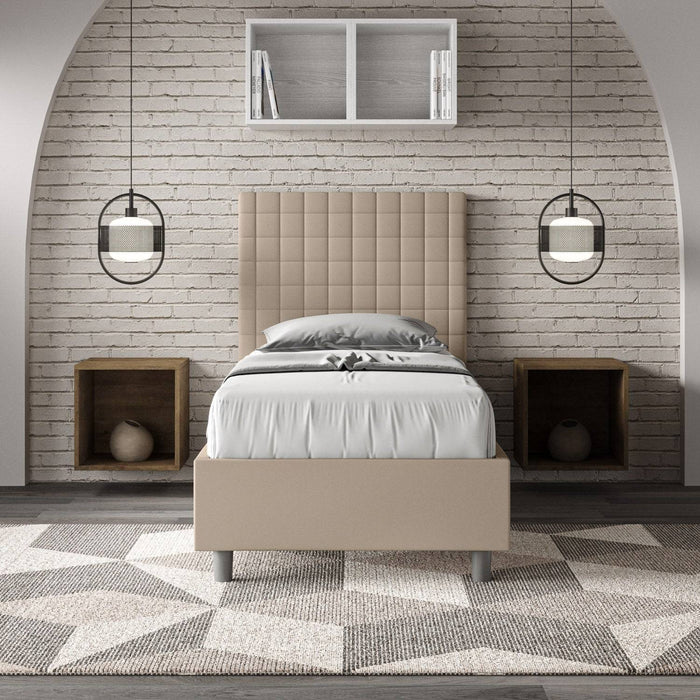 Letto singolo imbottito similpelle Sunny beige in camera moderna con parete in mattoni e comodini a incasso. Arredo raffinato e pratico.