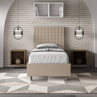 Letto singolo imbottito similpelle Sunny beige in camera moderna con parete in mattoni bianchi e arredamento geometrico.