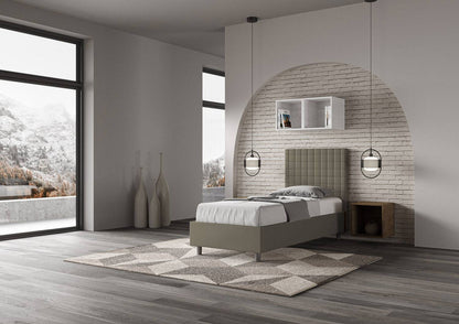 Letto singolo imbottito similpelle Sunny grigio scuro visto lateralmente in camera moderna con vista panoramica e design essenziale.