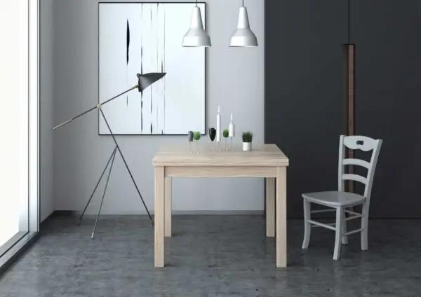 Tavolo allungabile color legno chiaro con gambe in massello e piano nobilitato 110/150x70 cm, in un ambiente moderno con lampada e sedia bianca.