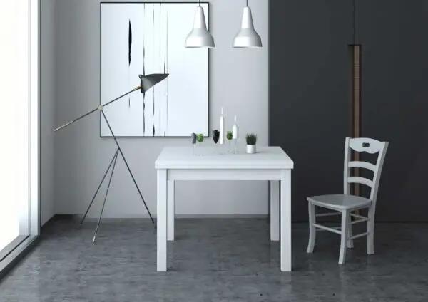 Tavolo allungabile bianco con gambe in massello e piano nobilitato 110/150x70 cm, in un ambiente moderno con lampada e sedia bianca.