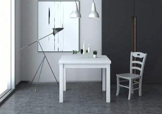 Tavolo allungabile bianco con gambe in massello e piano nobilitato 110/150x70 cm, in un ambiente moderno con lampada e sedia bianca.