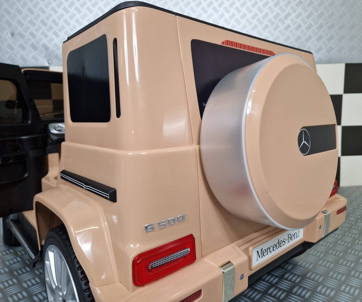 Interno dell'auto elettrica per bambini Mercedes G500, con volante in plastica, pannello di controllo con pulsanti e sedile in pelle nera con logo Mercedes.
