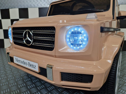 Vista frontale dell'auto elettrica per bambini Mercedes G500, con volante con logo Mercedes, luci LED blu e dettagli in plastica di alta qualità.