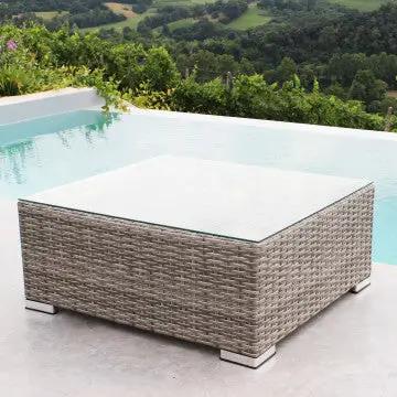Tavolino Copacabana in wicker grigio con piano in vetro, posizionato vicino a una piscina, perfetto per ambienti esterni eleganti.